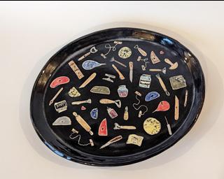 A handmade serving platter decorated with a variety of colorful pottery tools which have been carefully carved for added detail.