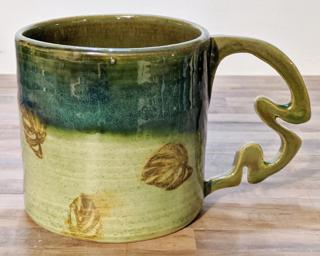 A lovely ceramic mug with little monstera leaves stamped around the outside and unique handle that is quite comfortable to hold.