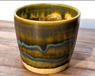 A small olive green and blue cup with an aurora-like glaze pattern on it.