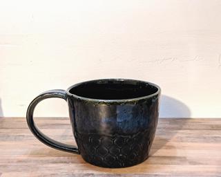 A hefty ceramic mug with a black scale pattern around the outside highlighted with a blue-purple sheen around the top.