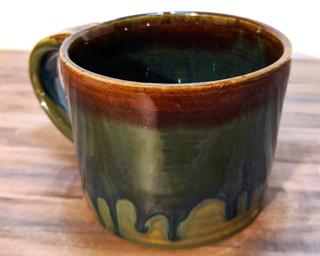 A hefty ceramic mug with a gorgeous  green and blue drip around the outside with a red ring around the top.
