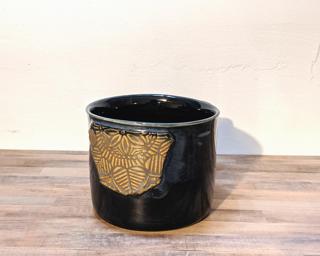 A hefty ceramic mug with a geometric applique attached to the side.