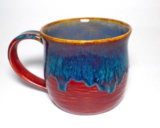 A hefty ceramic mug with a gorgeous drippy blue glaze over a textured red base on the outside and a blue interior.