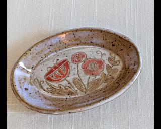 A small handmade oblong-shaped dish decorated with various colorful flowers which have been carefully carved for added detail.