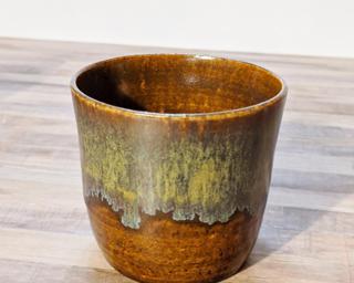 A small ceramic cup with cascading glazes around the outside.