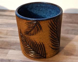 A small ceramic cup with carved pine leaves around the outside and a lovely mottled blue on the inside.