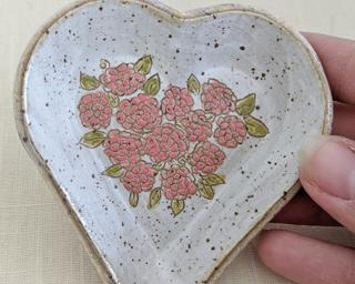 A small handmade heart-shaped dish decorated with a dozen little hand drawn carnations.