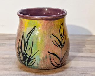 A very colorful ceramic mug with leaf designs painted around the outside.