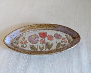 A handmade oblong-shaped dish decorated with various colorful flowers which have been carefully carved for added detail.
