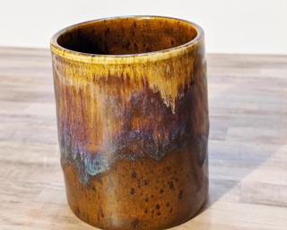 A small ceramic cup with cascading glazes around the outside.