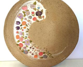A large handmade dish hand painted with various colorful flowers which have been carefully carved for added detail.