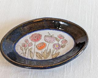 A small handmade oblong-shaped dish decorated with various colorful flowers which have been carefully carved for added detail.
