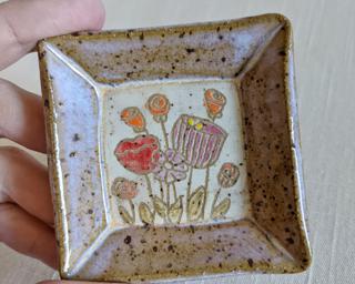 A little handmade square dish decorated with a variety of colorful flowers which have been carefully carved for added detail.