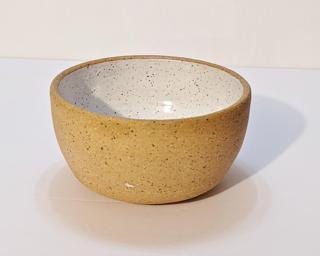A small handle-less ceramic cup with a white glaze over a mid-fire speckled clay.