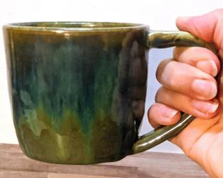 A hefty ceramic mug with a gorgeous  green and blue drip around the outside with a red ring around the top.