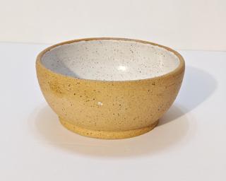 A small handle-less ceramic cup with a white glaze over a mid-fire speckled clay.